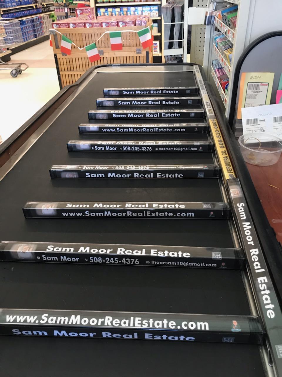 Sam Moor Real Estate branded dividers arranged on a checkout belt